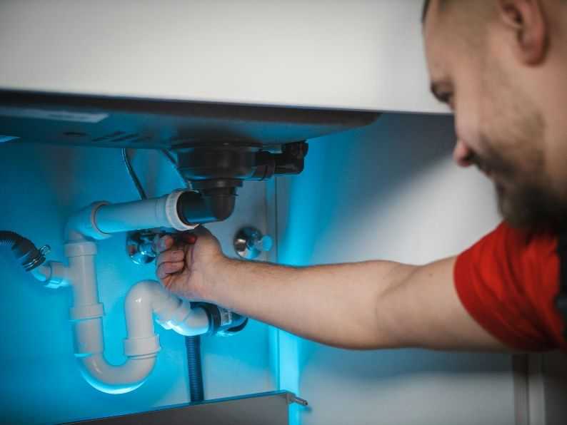 Plumber reaching into white cabinetry under sink and adjusting a water valve